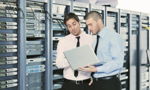 Two engineers working on a laptop in a server room