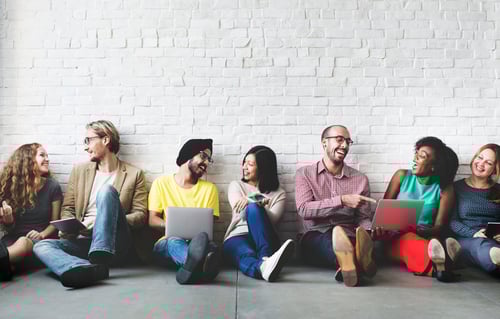 A group of 7 women and men sit on the floor and talk together.