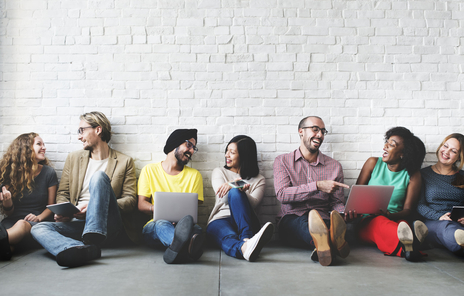 A group of 7 women and men sit on the floor and talk together.