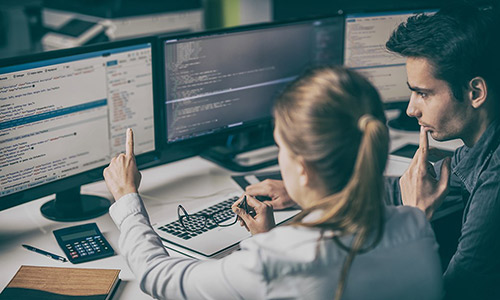 A woman and a men are working together on a double screen computer.